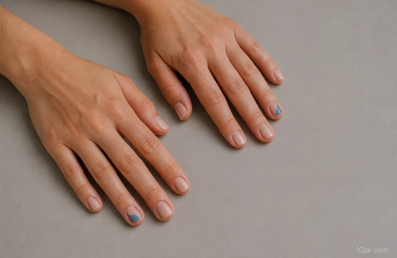 Two natural adult hands with short rosy neutral nails and one muted-blue diagonal accent per hand on a plain surface