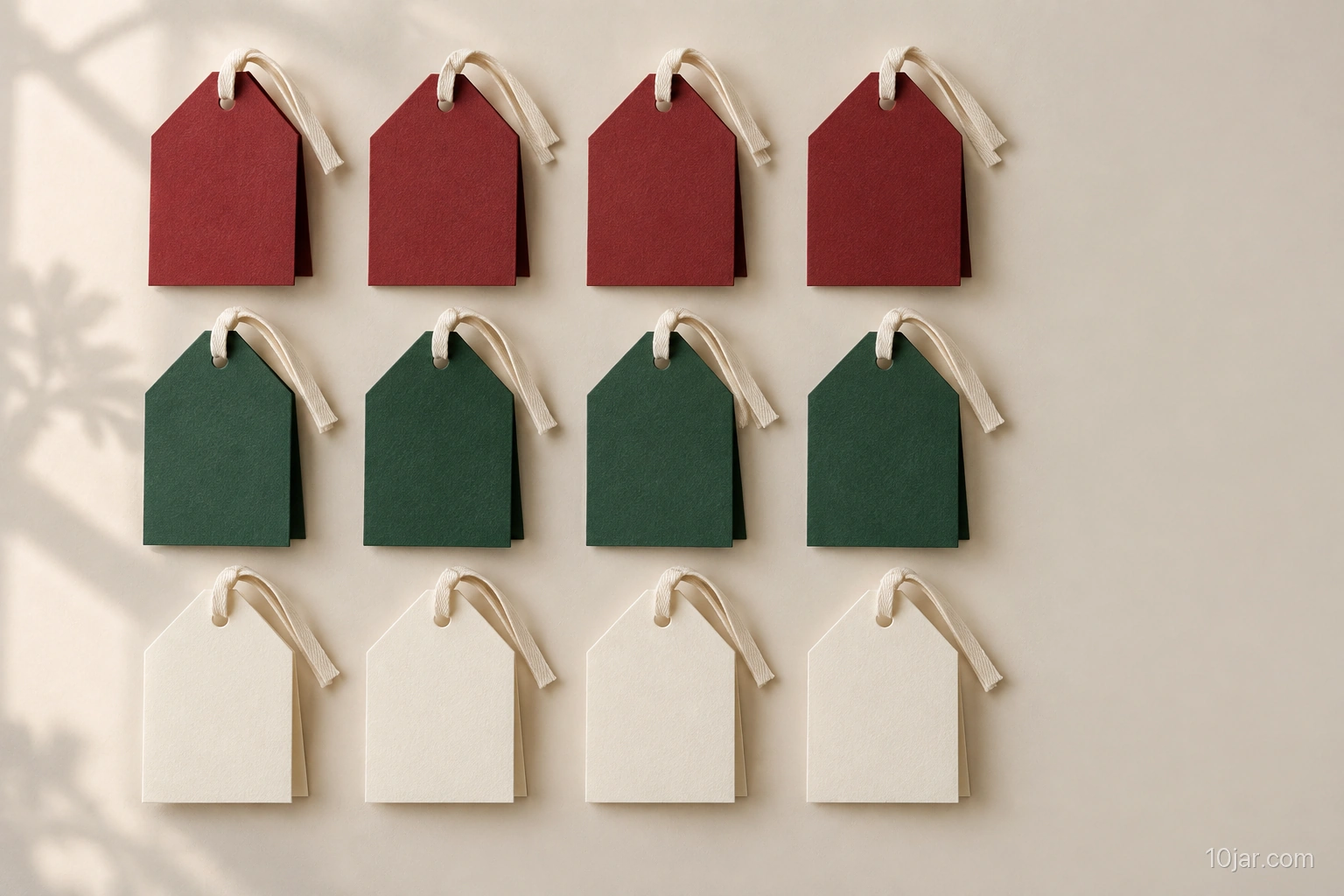 Exactly twelve folded red green and cream paper house gift tags with punched ribbon loops arranged in three neat rows